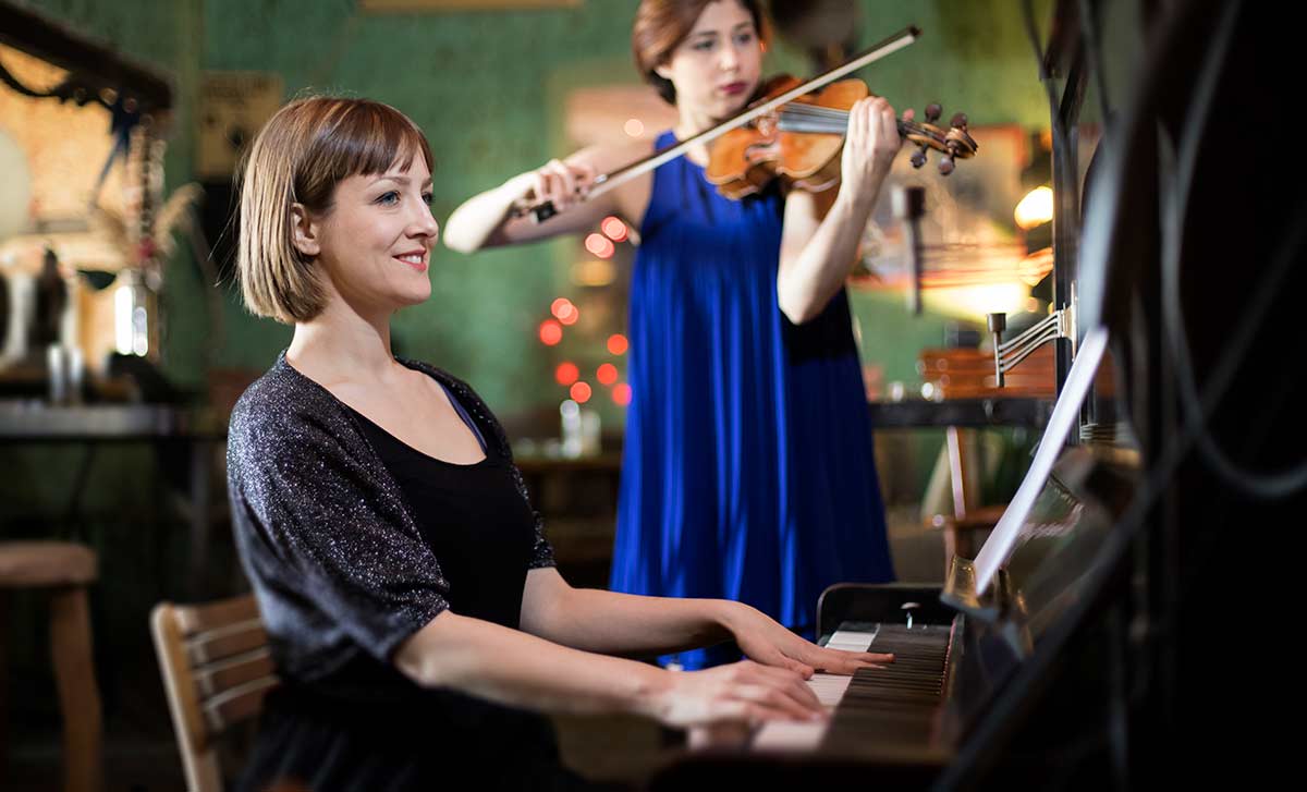 A woman playing piano with a violinist
