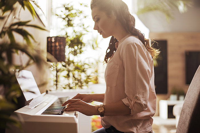 Beautiful woman playing digital piano at home