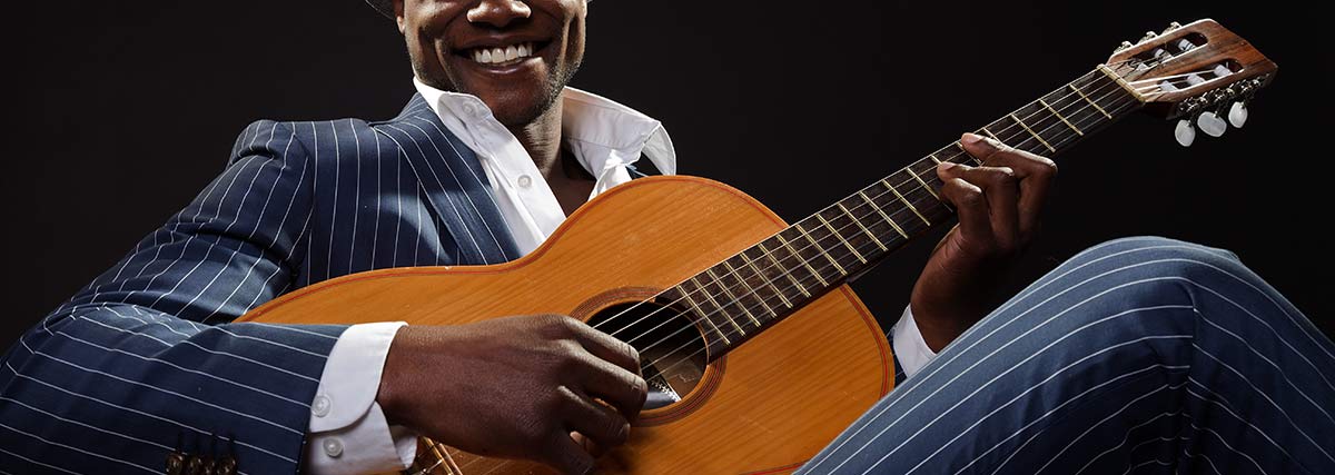 Black jazz musician wearing suit and grey hat playing guitar