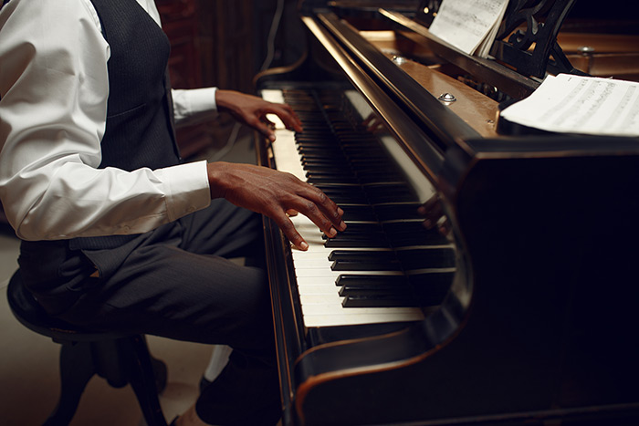 Black man wearing a vest playing the piano