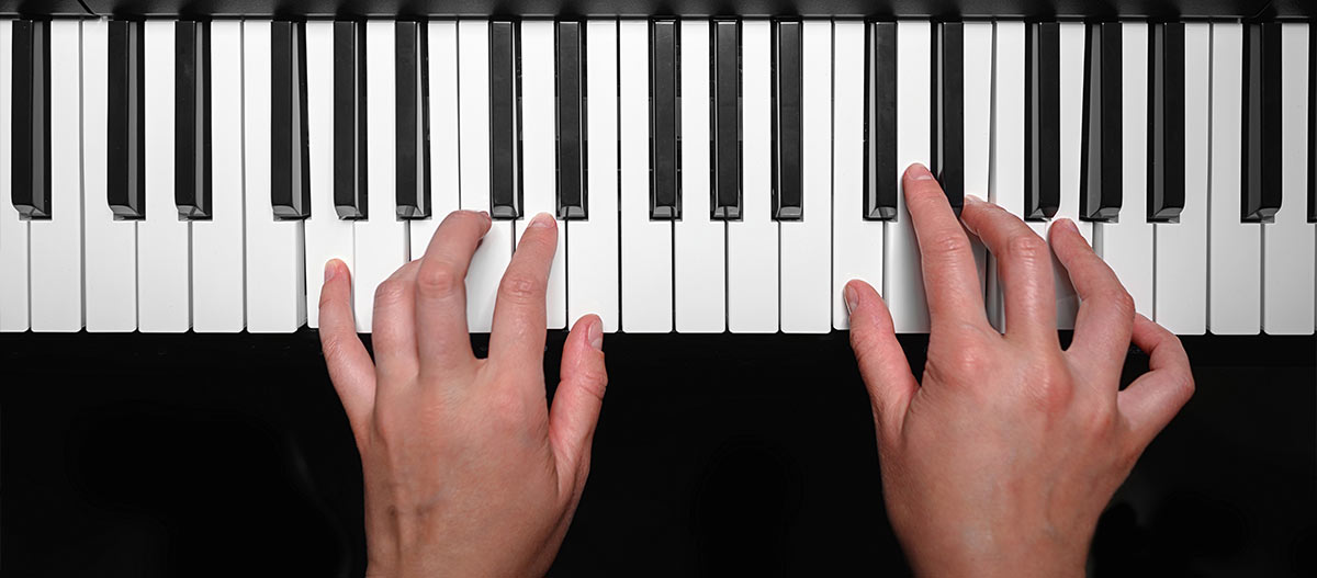 Close up of hands playing a C major chord on a digital piano keyboard