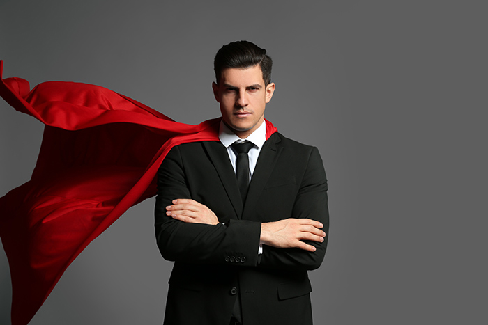 Serious l ooking man wearing suit with superhero red color cape on grey background feat
