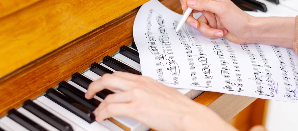 Woman hands writing on music sheet while playing piano