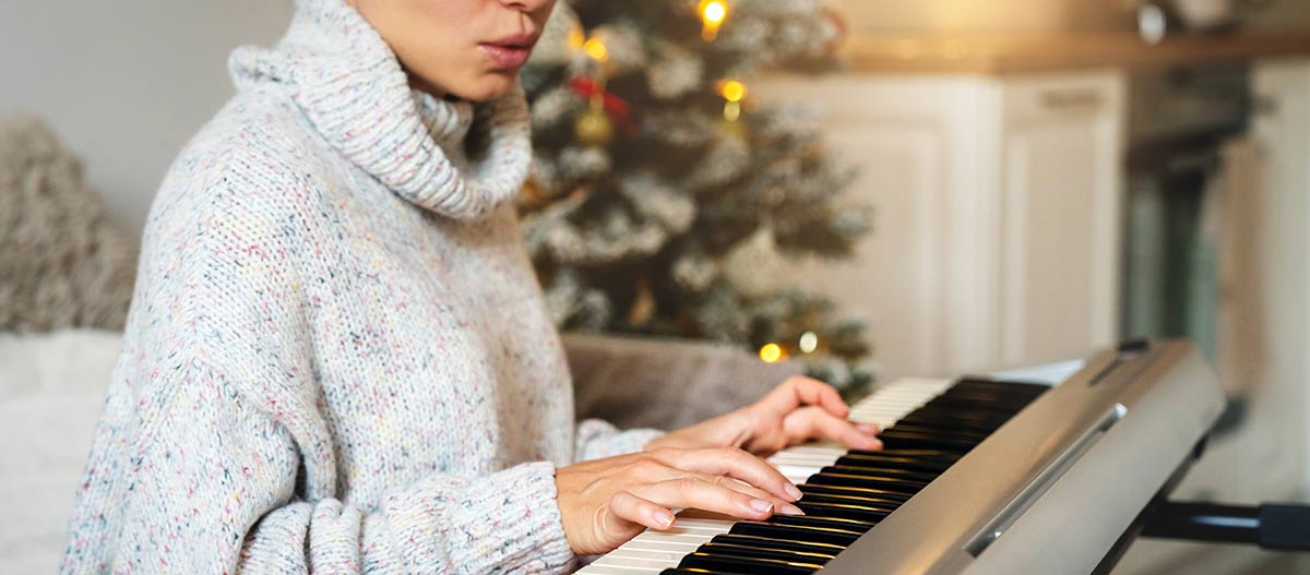 Woman playing digital piano near Christmas tree