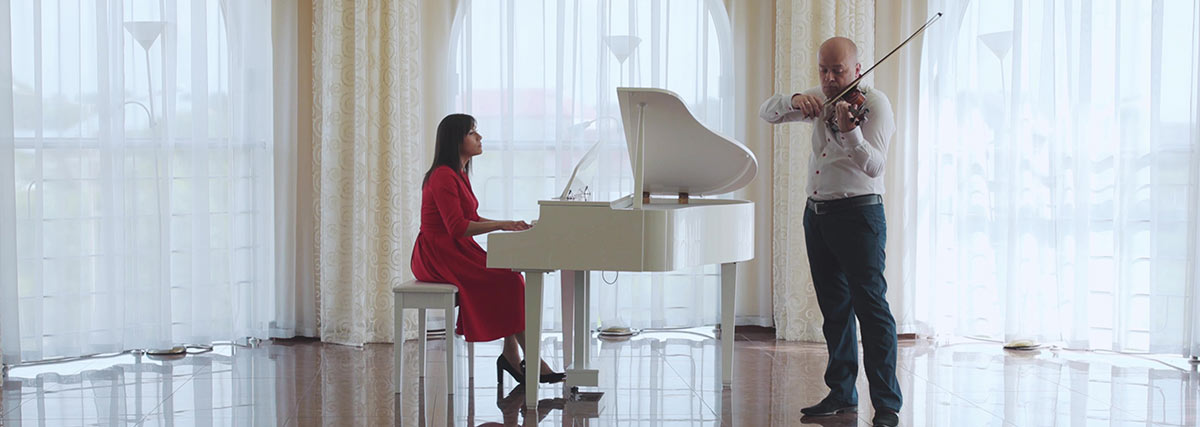 Woman playing piano and man playing violin together